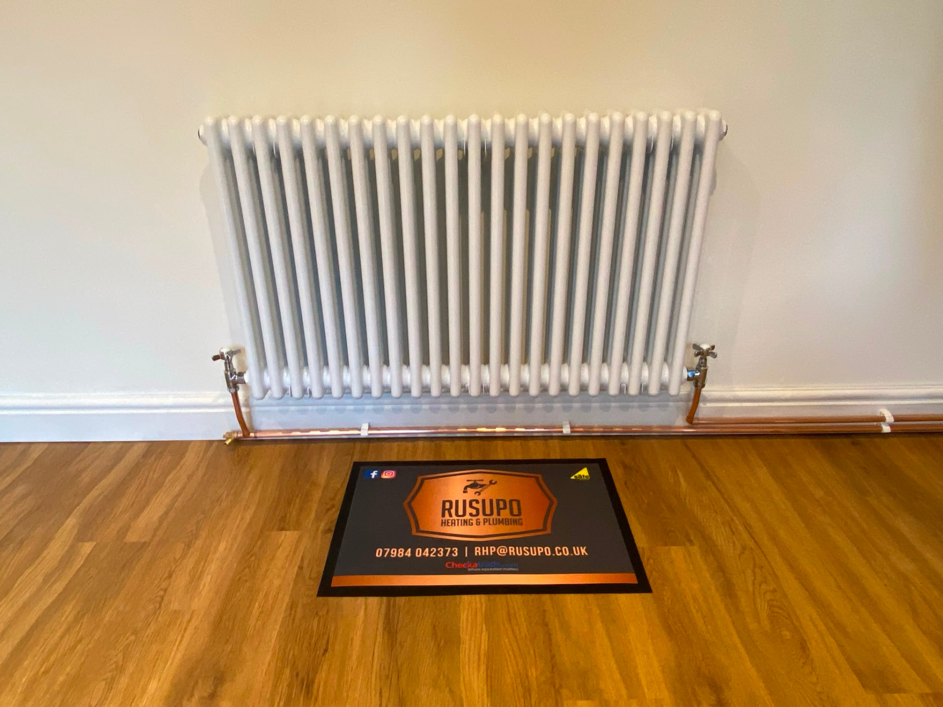 New white vertical column radiator installation on a wooden floor, fitted by Gas Safe registered engineers in Essex